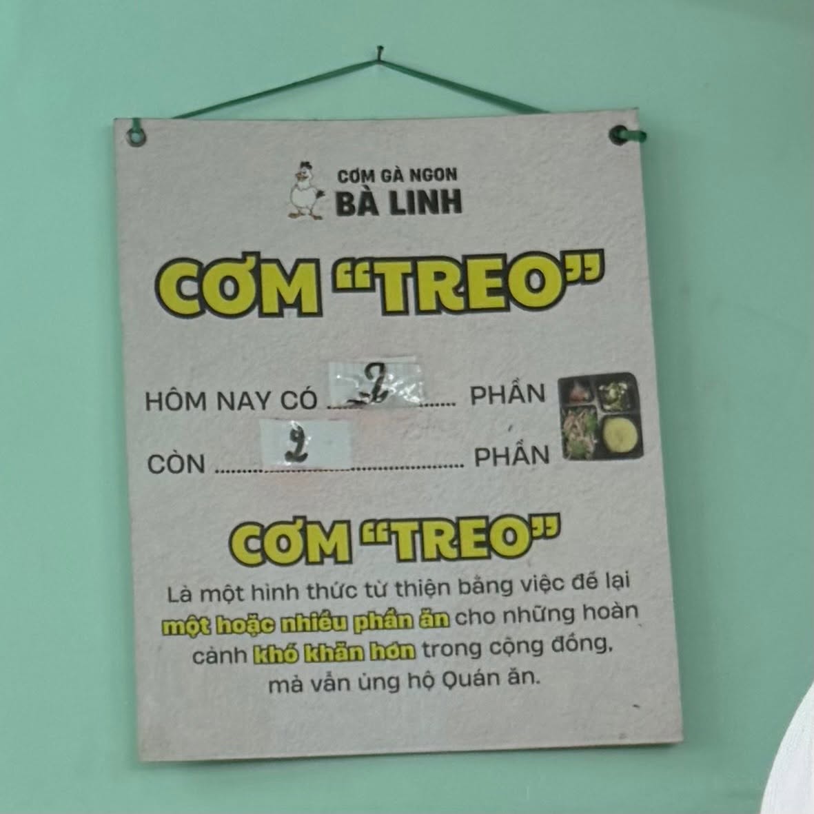 Bảng cơm treo của quán Cơm Gà Ngon Bà Linh, ghi hôm nay có 2 phần, còn 2 phần, giải thích cơm treo là để lại phần ăn cho người khó khăn hơn mà vẫn ủng hộ quán